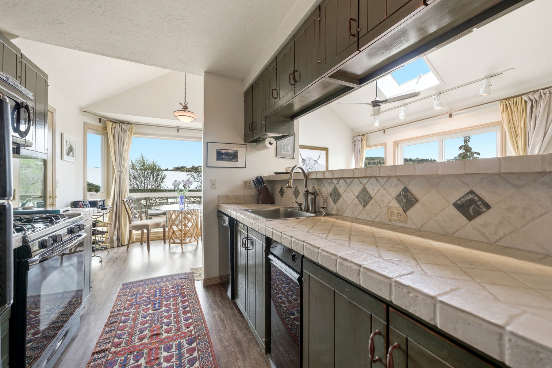 Kitchen featuring lofted ceiling, black range with gas cooktop, track lighting, a skylight, and tile countertops