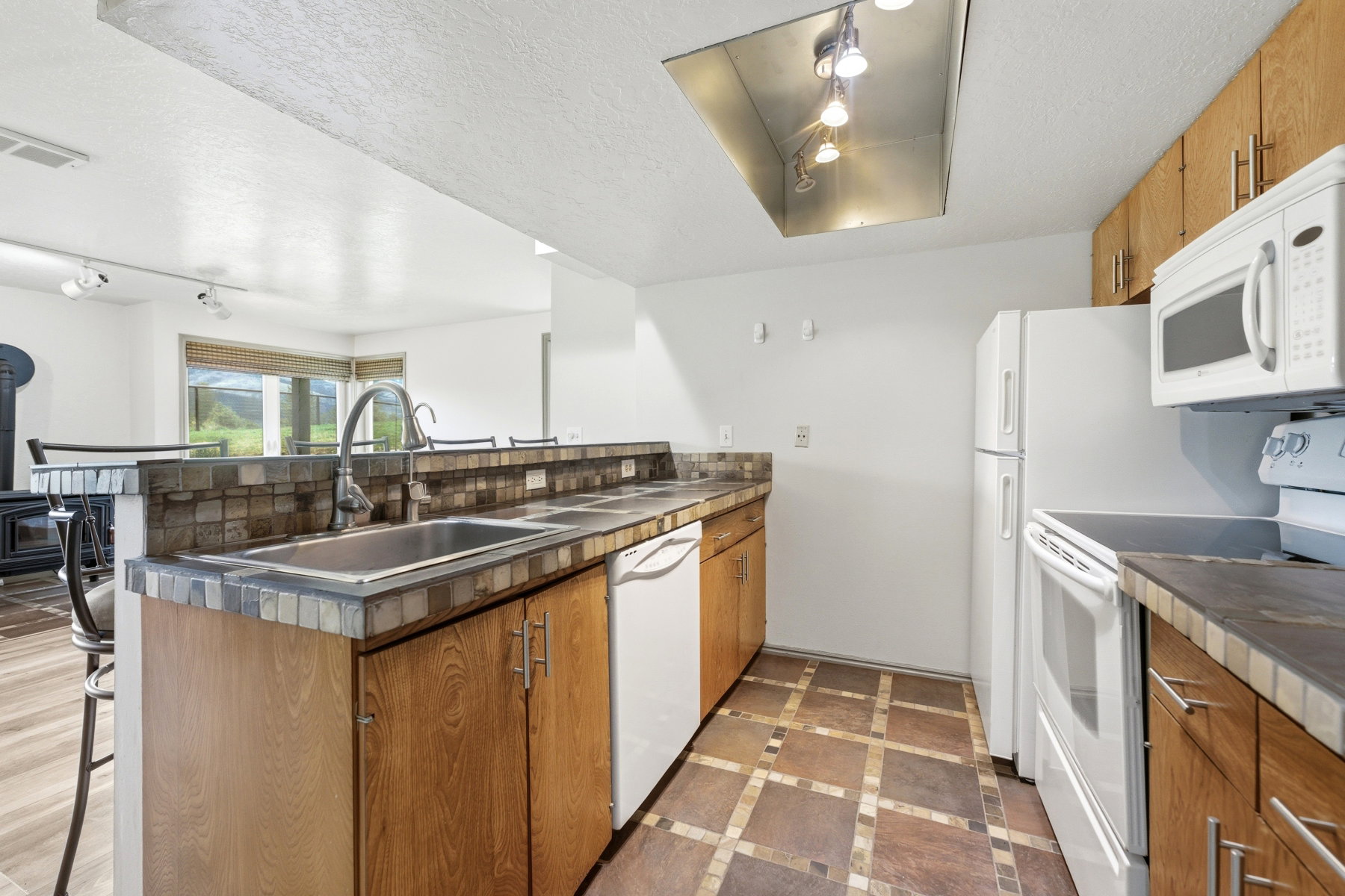 Kitchen featuring rail lighting, wood finish cabinetry, white appliances, dark countertops, and a kitchen breakfast bar