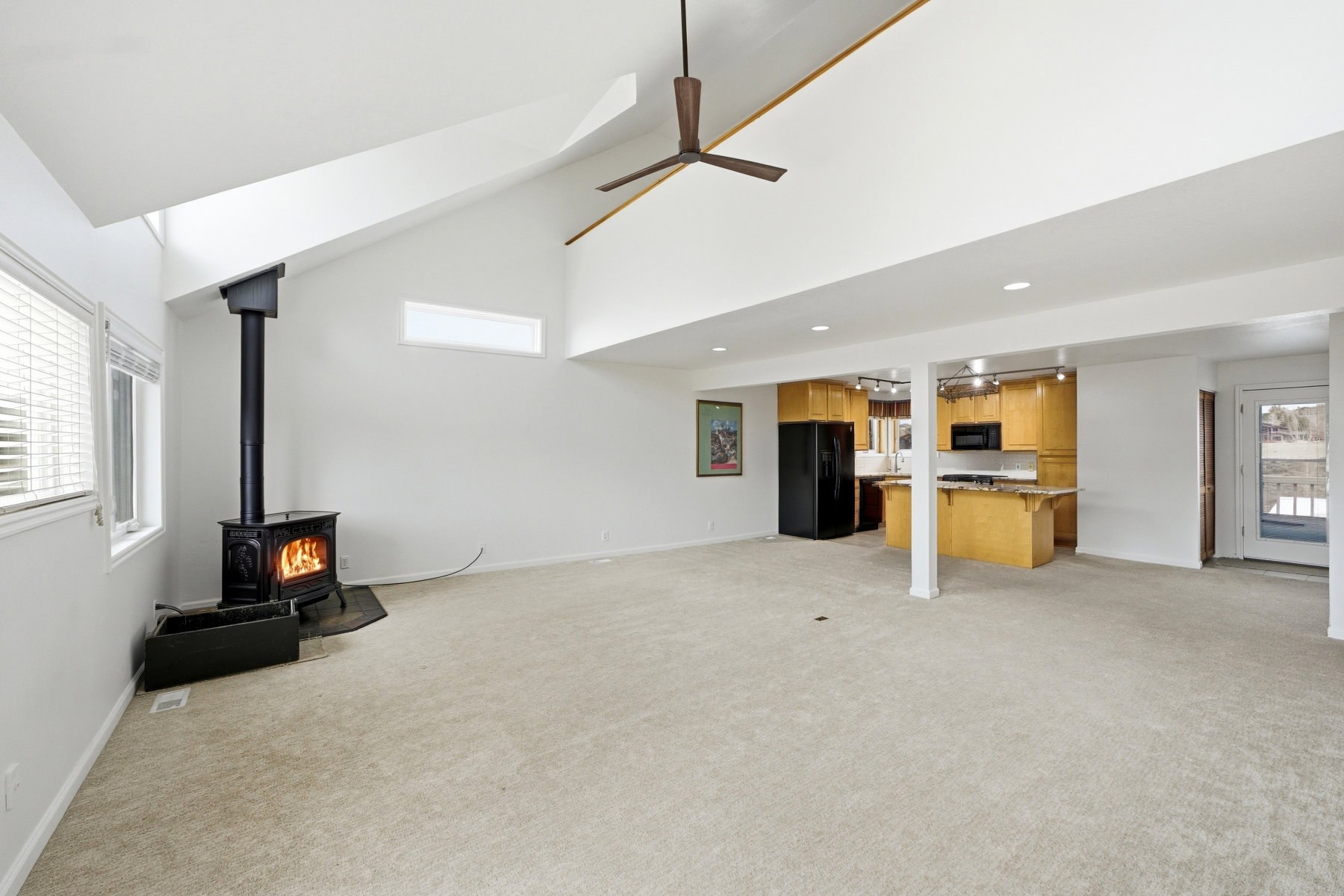 Unfurnished living room with a wood stove, light carpet, ceiling fan, recessed lighting, and lofted ceiling