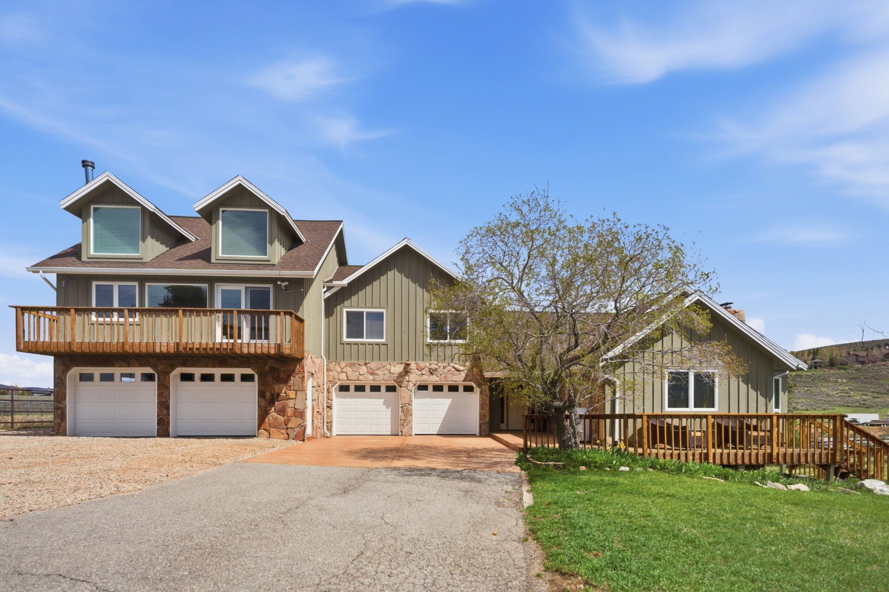 View of front facade featuring board and batten siding, an attached garage, asphalt driveway, stone siding, and a wooden deck