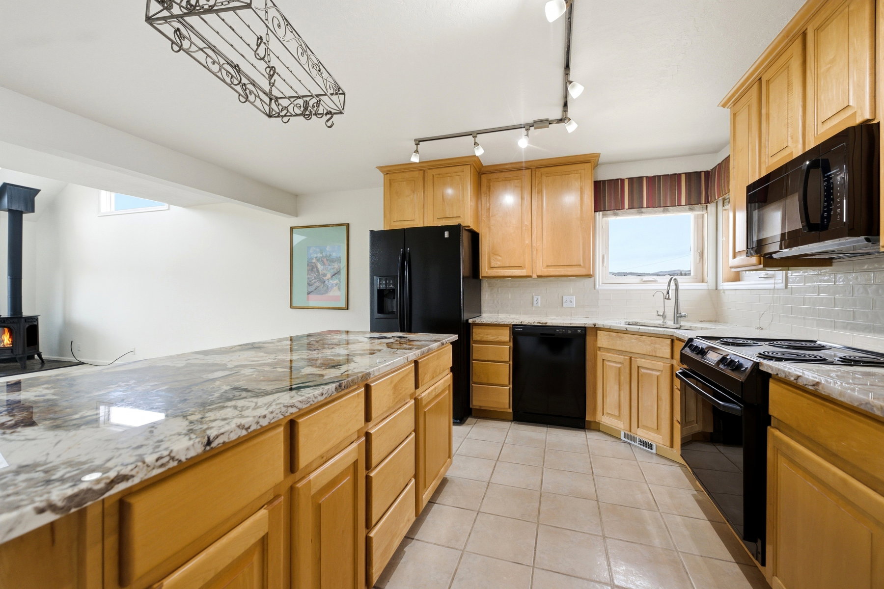 Kitchen featuring black appliances, light stone counters, and tasteful backsplash