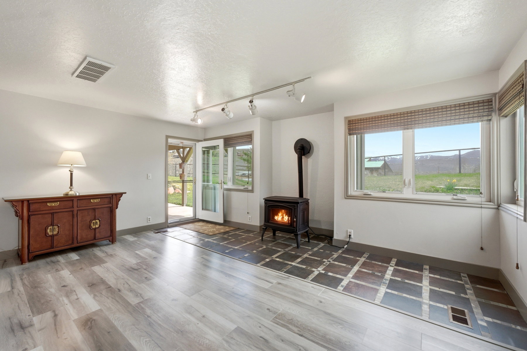 Living room with a textured ceiling, a wood stove, track lighting, light wood-style floors, and healthy amount of natural light