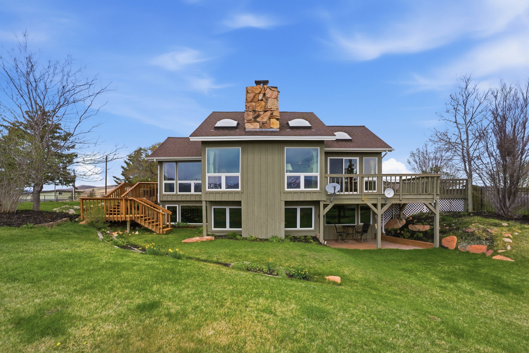 Rear view of house featuring a wooden deck, a chimney, a patio, roof with shingles, and a yard