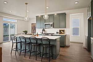 Kitchen featuring a kitchen bar, an island with sink, decorative light fixtures, and dark wood-style floors