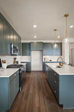 Kitchen with stainless steel appliances, dark wood-type flooring, decorative light fixtures, and light stone counters