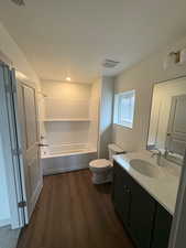 Bathroom with vanity, dark wood finished floors, shower / bath combination, and a textured ceiling