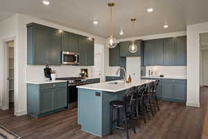 Kitchen featuring stainless steel appliances, a kitchen breakfast bar, dark wood-style flooring, and a center island with sink