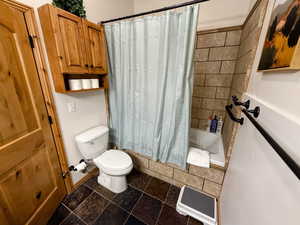 Full bathroom featuring shower / bathtub combination with curtain and stone tile floors