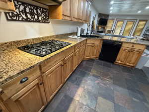 Kitchen with light stone countertops, a peninsula, black appliances, stone tile flooring, and open floor plan