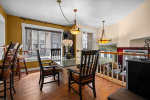 Dining area with real wood flooring, open banister, dining table/chairs, and granite bar.