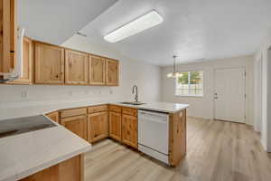 Kitchen with light wood finish cabinetry, a peninsula, dishwasher, and suspended lighting