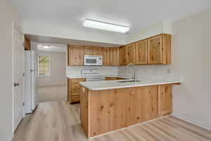 Kitchen featuring light countertops, a peninsula, white appliances, light wood-style flooring, and light wood finish cabinets