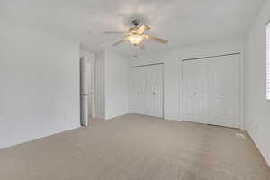 Unfurnished bedroom featuring two closets, light colored carpet, and ceiling fan