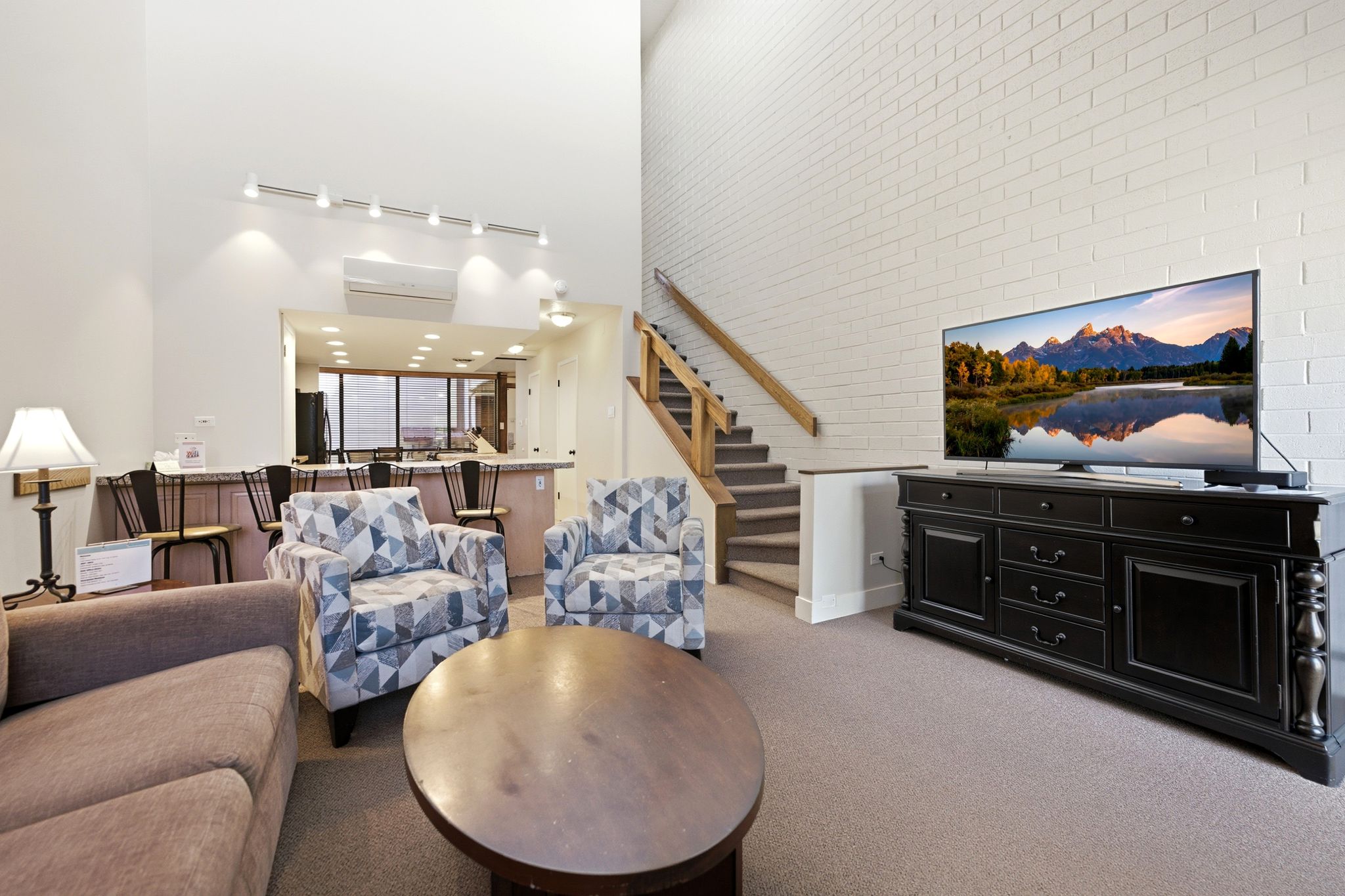 Two-story living area featuring a brick accent wall, track lighting, and a built-in breakfast bar with seating
