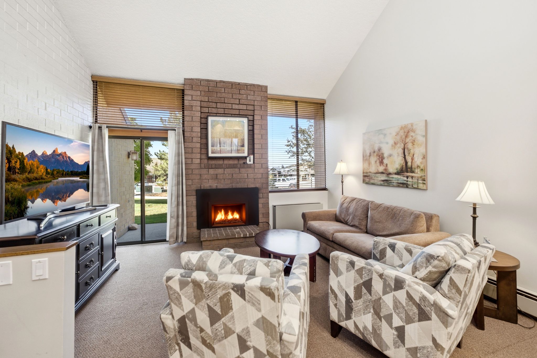 Living area featuring vaulted ceilings, a brick-surround fireplace with hearth, and durable carpet flooring