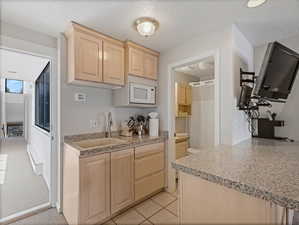 Kitchen featuring light wood finish cabinetry, a textured ceiling, white microwave, a baseboard radiator, and light tile patterned flooring