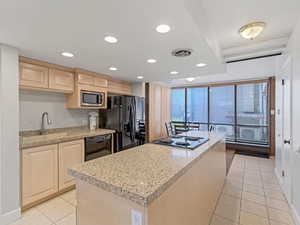 Kitchen with light wood finish cabinetry, recessed lighting, a kitchen island, black appliances, and light tile patterned floors