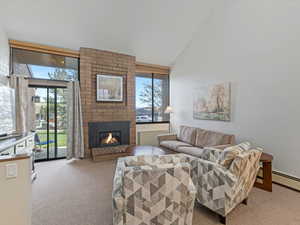 Living area with light carpet, lofted ceiling, and a brick fireplace