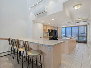 Kitchen featuring a kitchen breakfast bar, light wood finish cabinets, a peninsula, light tile patterned floors, and a center island