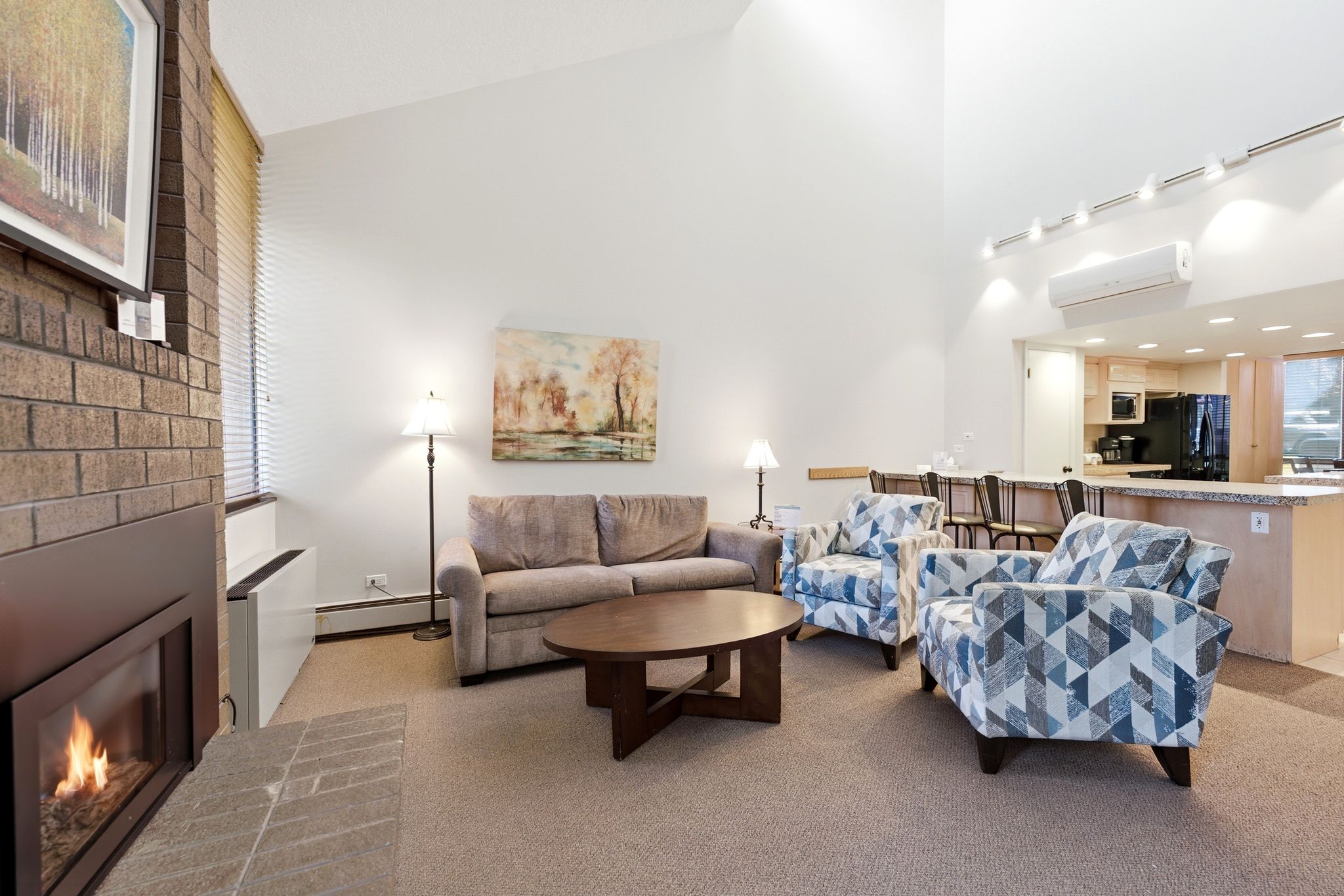 Vaulted ceilings enhance this living area featuring a brick fireplace, track lighting, and carpet flooring