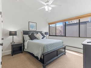 Bedroom featuring vaulted ceiling, baseboard heating, a ceiling fan, and light colored carpet