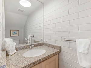 Half bathroom featuring vanity, vaulted ceiling, and concrete block wall