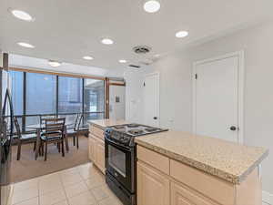 Kitchen featuring black appliances, light countertops, light carpet, light wood finish cabinetry, and a center island