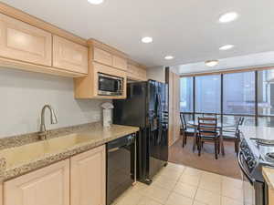 Kitchen featuring black appliances, light wood finish cabinetry, light stone countertops, recessed lighting, and floor to ceiling windows