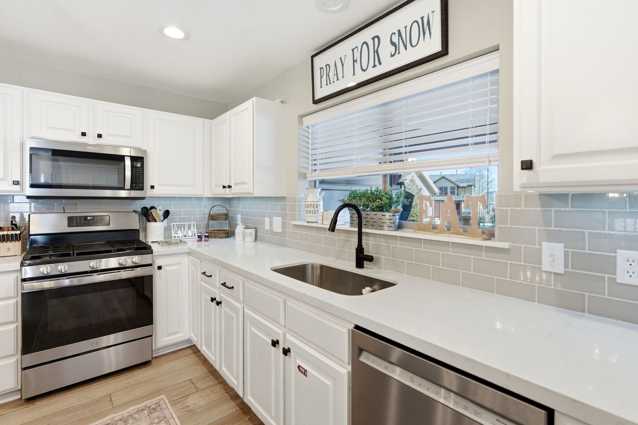 Kitchen with stainless steel appliances, light stone countertops, white cabinets, light wood-style flooring, and backsplash