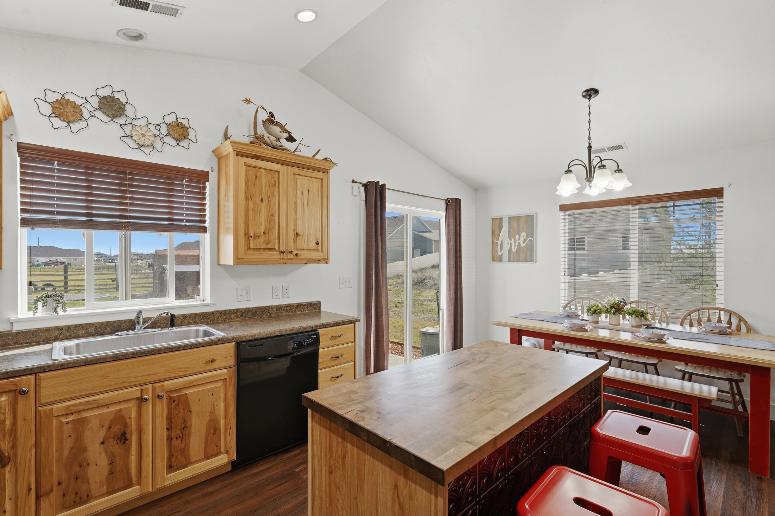 Kitchen featuring a center island, vaulted ceiling, black dishwasher, dark wood-style floors, and hanging lights