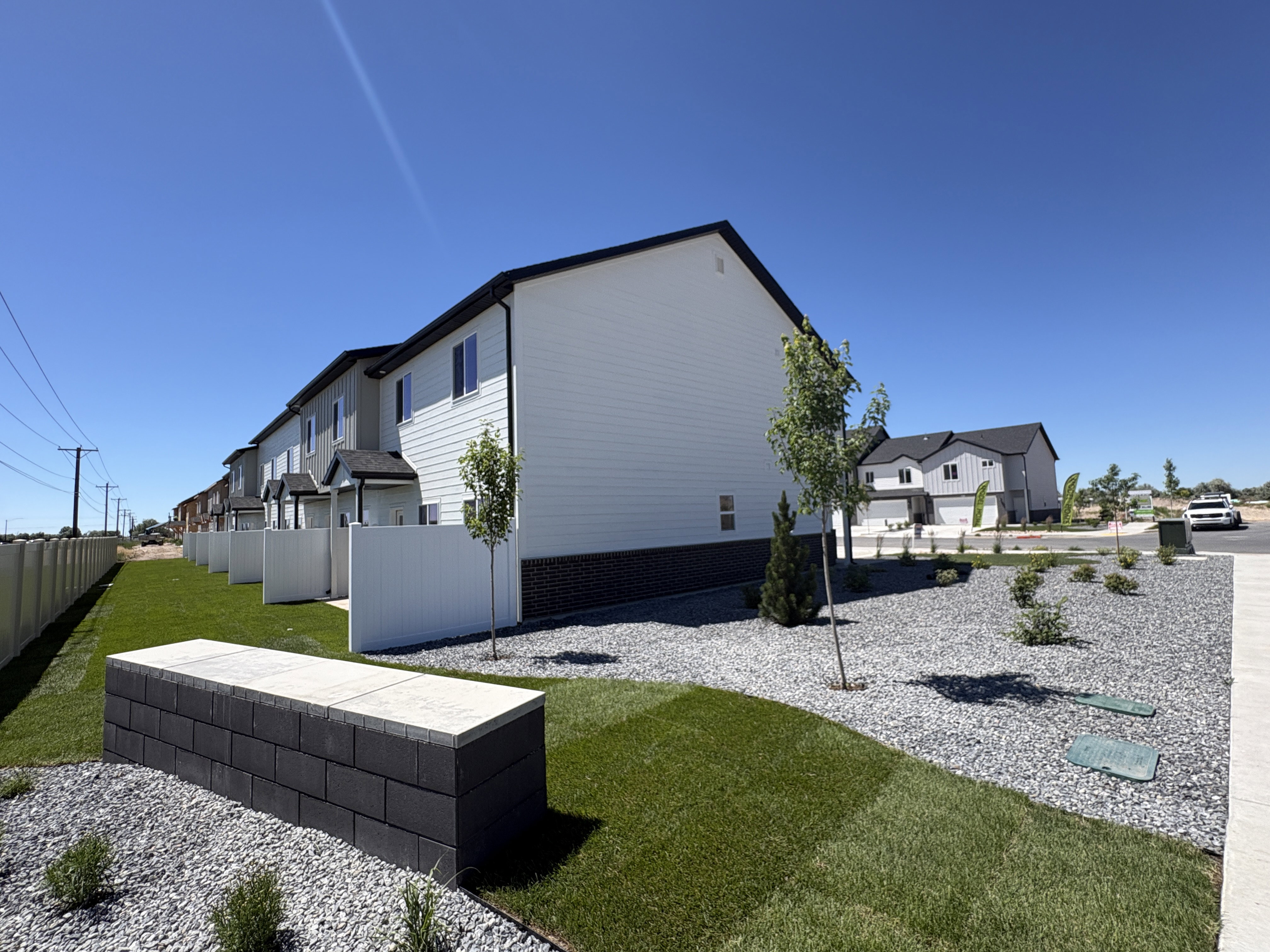 Contemporary row of properties featuring white siding with dark trim, individual fenced patio areas, and a well-maintained lawn