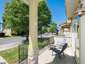 Covered front porch featuring a stone and painted column, black wrought iron railing, and a concrete surface