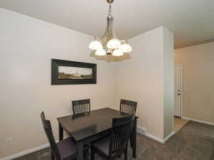 Dining area featuring a brushed nickel chandelier with frosted glass shades, neutral wall paint, white trim, and textured carpeting