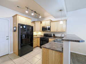 Kitchen featuring wood cabinetry, stainless steel microwave, black appliances, track lighting, and a breakfast bar with a pendant light fixture