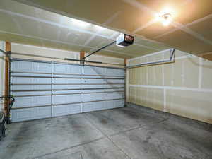 Attached garage featuring a panel-style garage door, concrete flooring, exposed wood framing, and ceiling-mounted lighting
