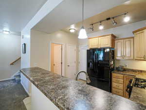 Kitchen featuring a multi-tone countertop peninsula, light wood-finish cabinetry, a black refrigerator, and a gas range
