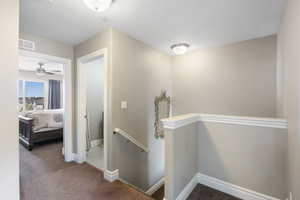 Corridor with an upstairs landing, dark carpet, and a textured ceiling