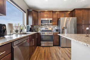 Kitchen with stainless steel appliances, light stone countertops, dark wood-style flooring, decorative backsplash, and recessed lighting