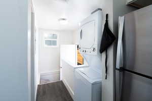 Laundry area with stacked washing machine and dryer and dark wood-style flooring.