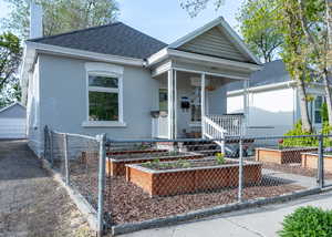 View of front of home featuring garden beds, a covered porch, chain link fence, and painted brick