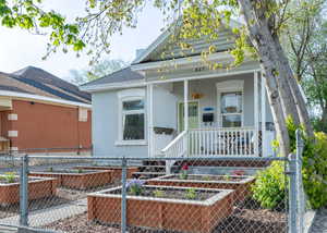 View of front of home featuring garden beds, a covered porch, chain link fence, and painted brick