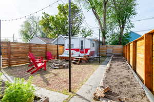 Fenced backyard featuring an outdoor fire pit, a patio, included retro camper, a detached garage, and garden beds.