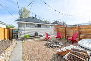 Rear view of house featuring a fenced backyard, a fire pit, & garden beds.