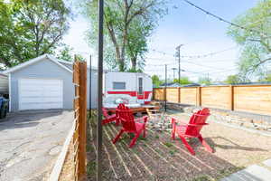 Fenced backyard featuring an outdoor fire pit, a patio, included retro camper, a detached garage, and driveway.