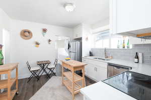 Kitchen with white cabinetry, backsplash, dark wood-type flooring, stainless steel appliances, and light quartz countertops