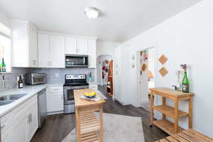Kitchen with white cabinetry, backsplash, dark wood-type flooring, stainless steel appliances, and light quartz countertops