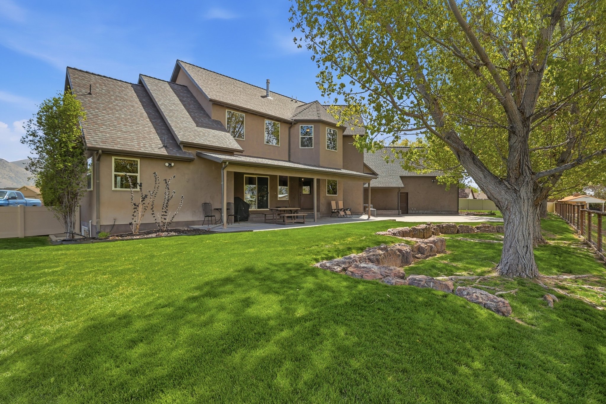 Expansive rear yard featuring a large green lawn, mature trees, and a rock-lined garden bed