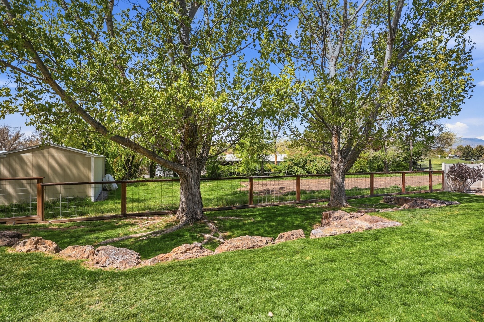 Expansive green lawn with mature trees, a wood and wire fence, and natural rock landscaping