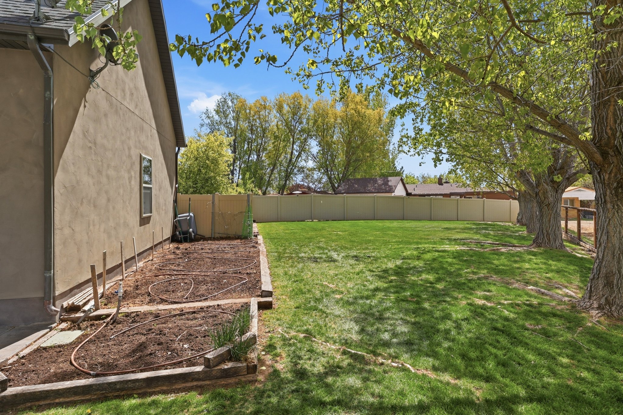 Expansive green lawn framed by mature trees, privacy fencing, and a dedicated garden bed