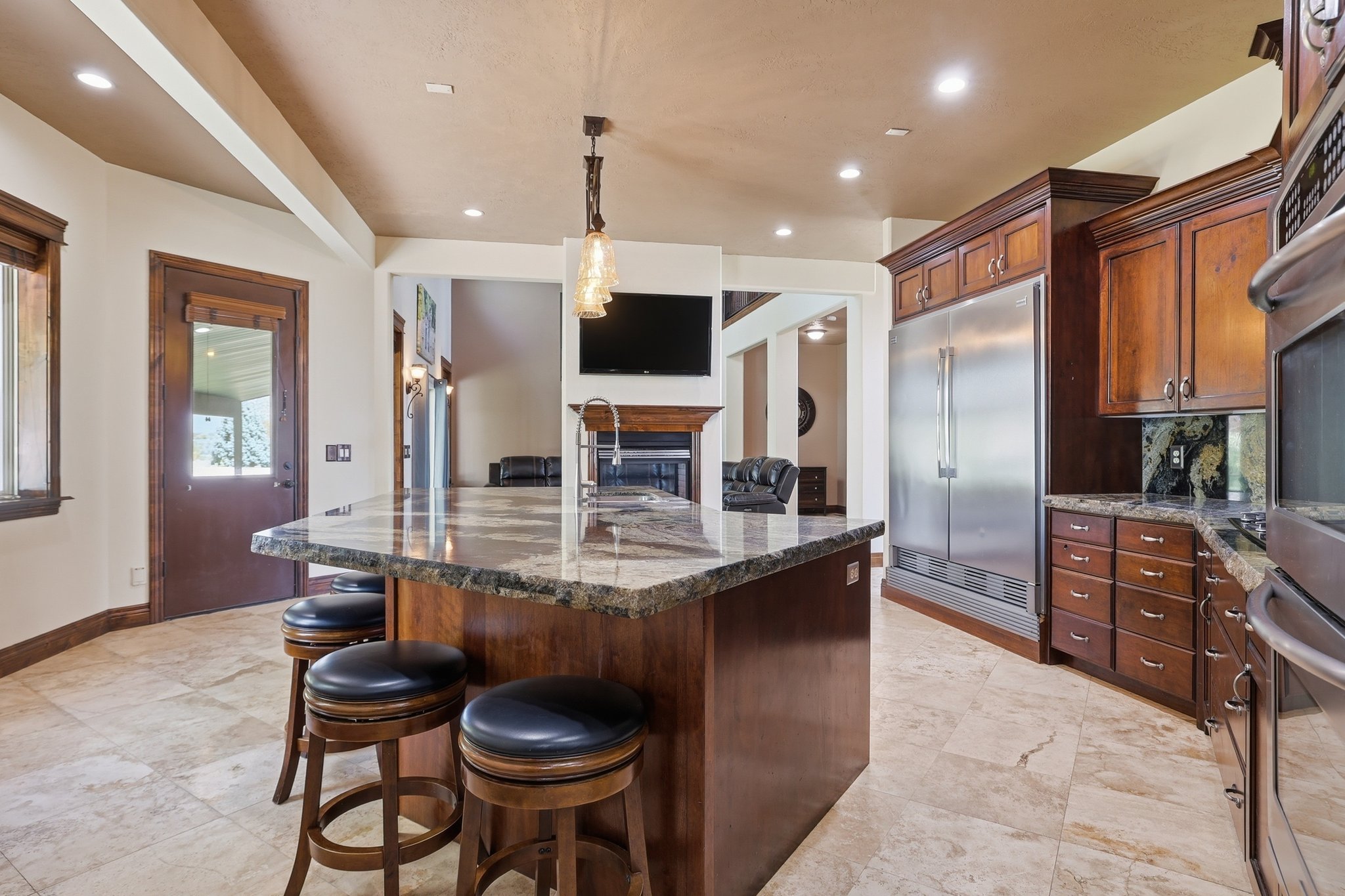 Spacious kitchen featuring a large island with stone countertop, rich wood cabinetry, stainless steel refrigerator, and built-in oven